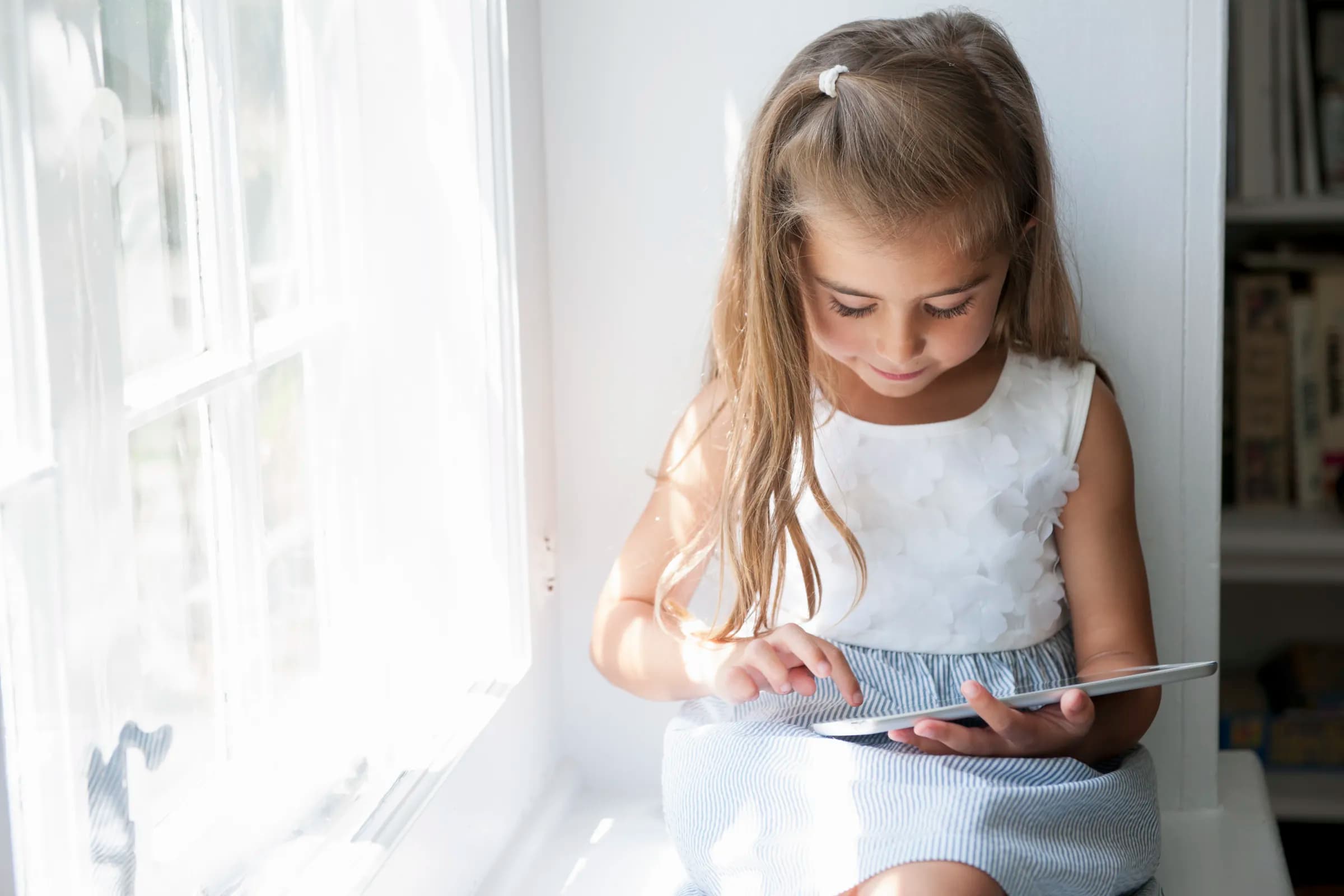 Girl sitting in a window seat at home, using a tablet